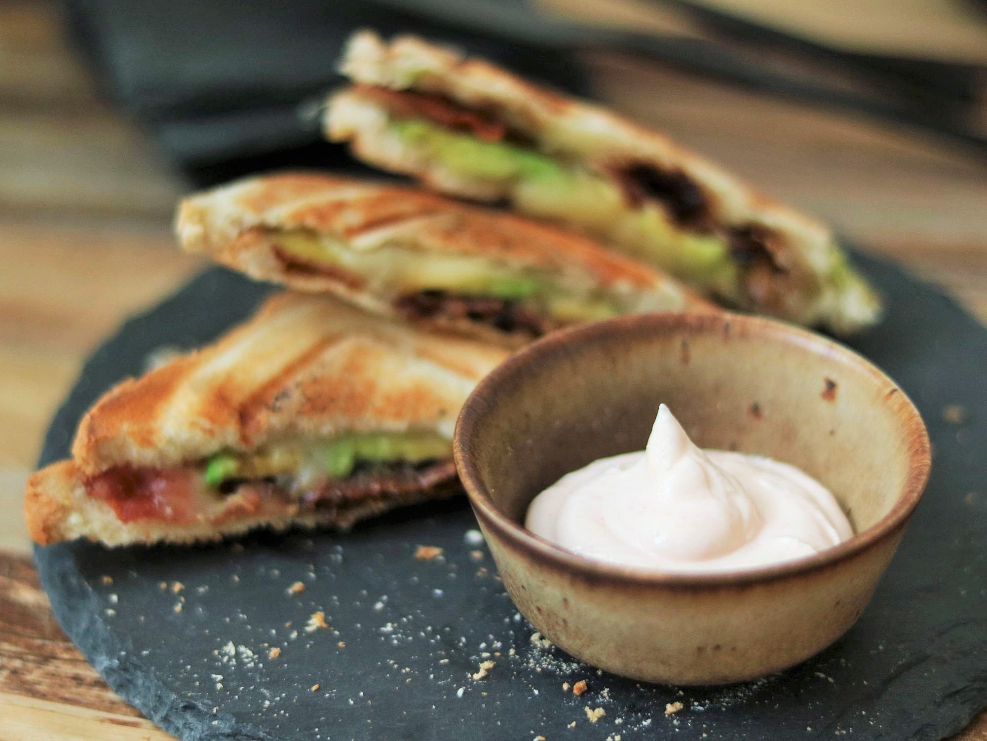 Bacon-Avocado-Sandwich wird in die Aioli getaucht