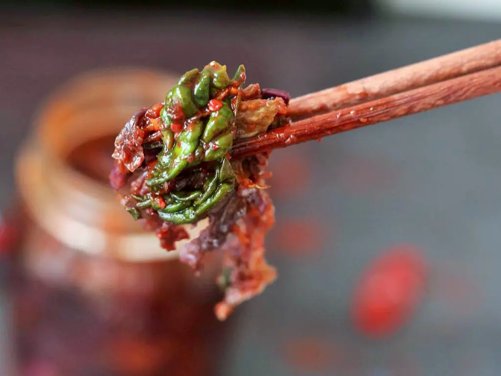 Chinesische Stäbchen, die Kimchi aus einem Glas eingeklemmt haben