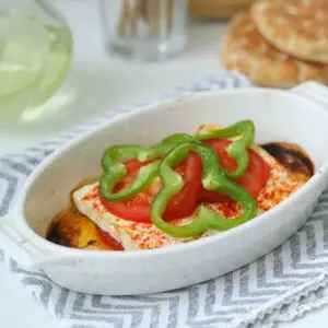 Gebackener Feta in einer weißen Auflaufform mit Tomatenscheibe und grüner Paprika