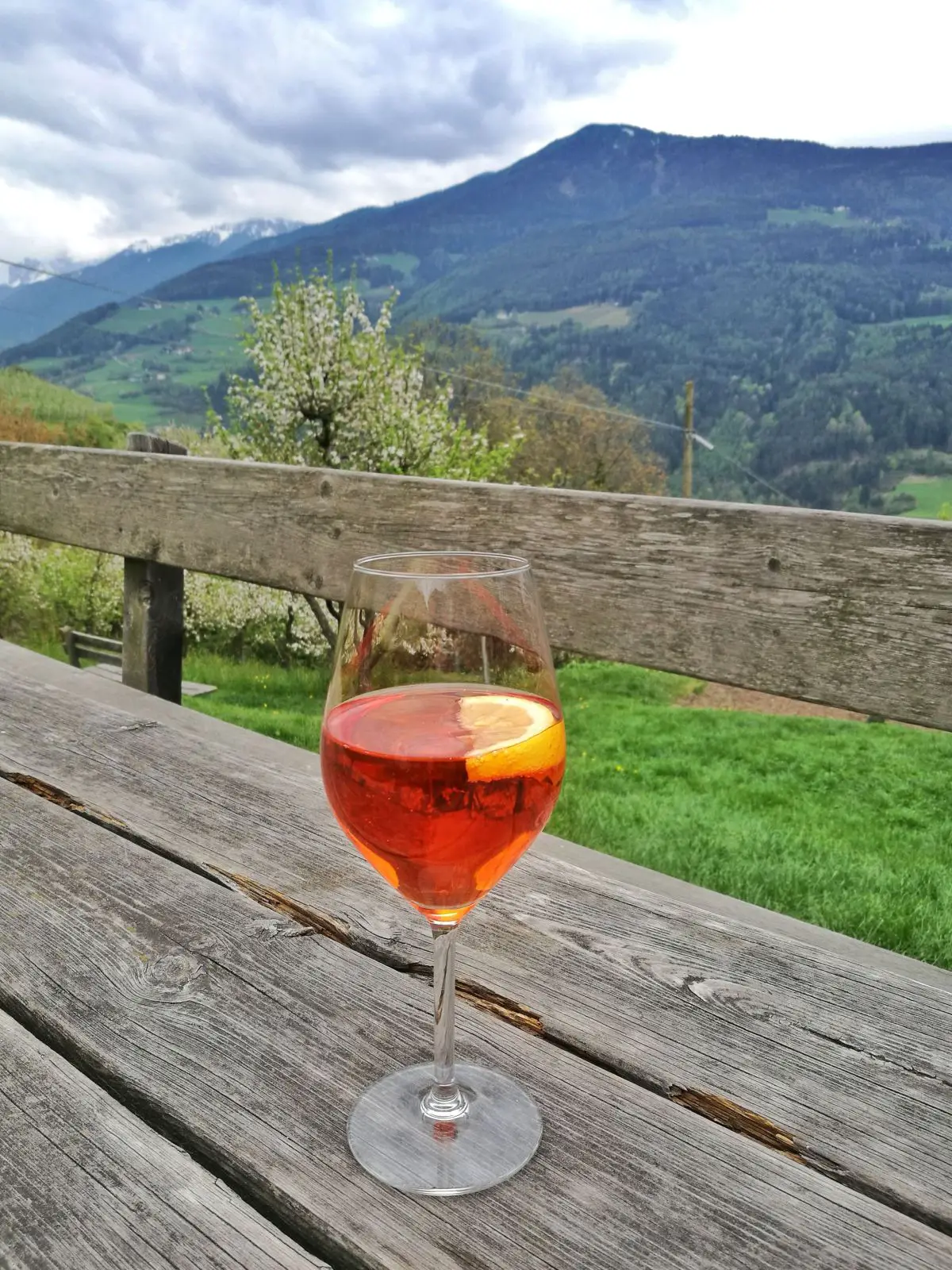 Glas Aperol Spritz auf einem Holztisch mit Blick in die Berge