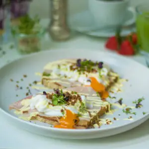 Pochierte Eier mit Senfcreme auf weißem Teller, im Hintergrund ein grüner Smoothie