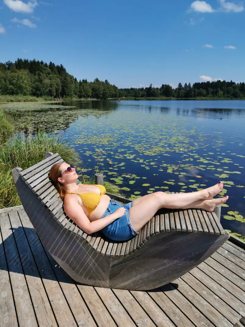 Frau liegt auf einem Holzschaukelstuhl am See