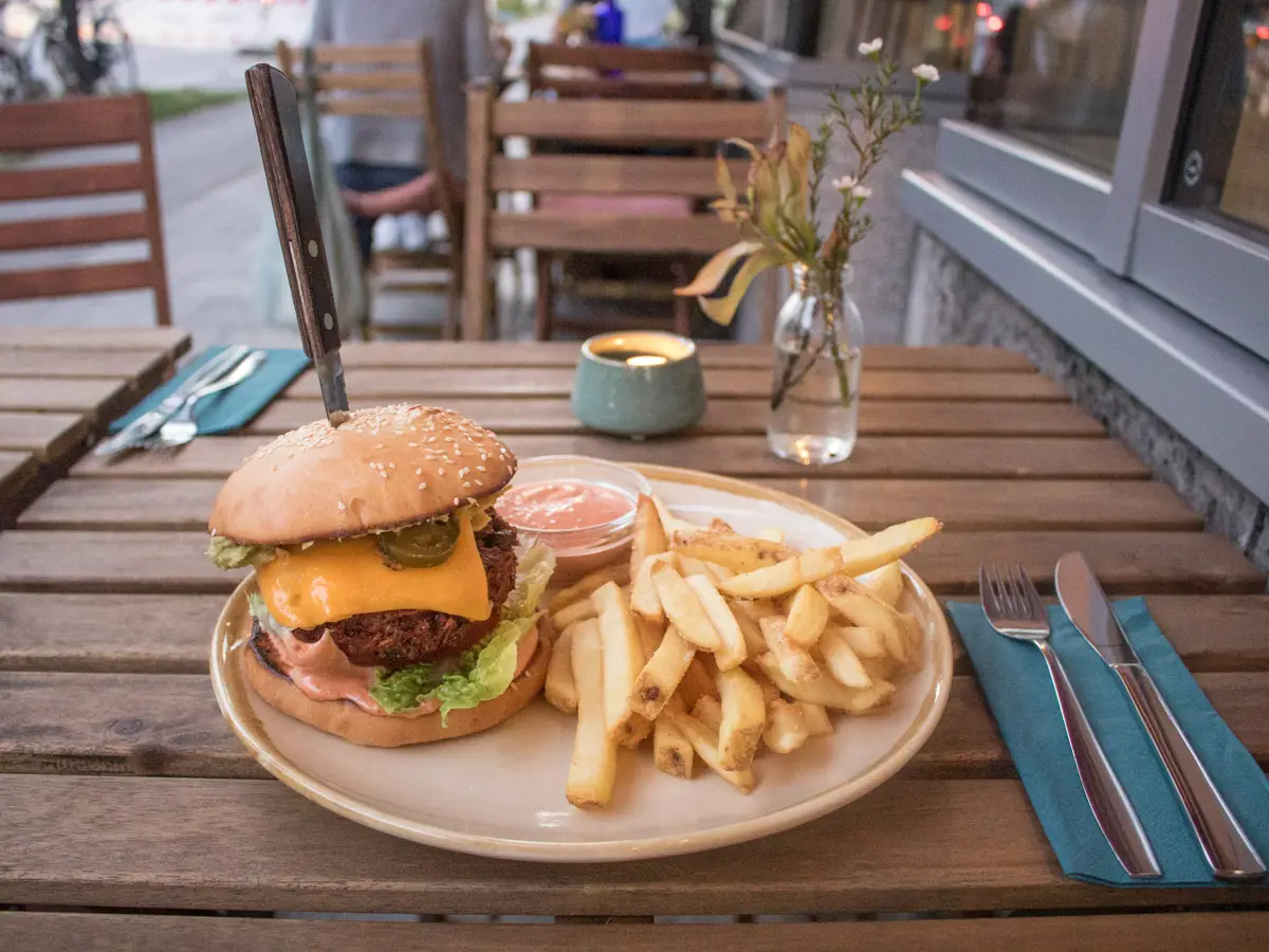 Emmi's Kitchen Holztisch mit einem Teller auf dem ein veganer Burger und Pommes liegen