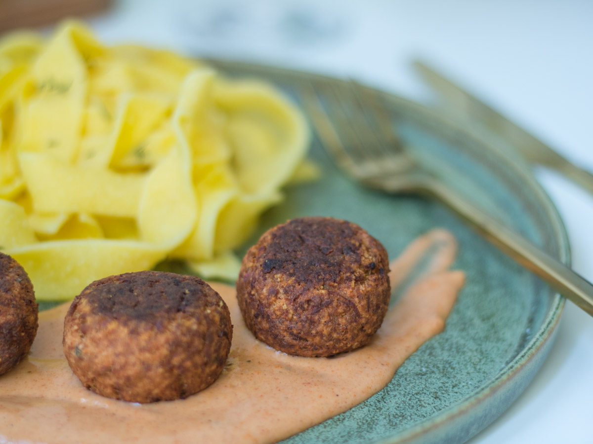 Nahaufnahme von 2 vegetarischen Kürbisbällchen auf einem Klecks Schlemmersauce