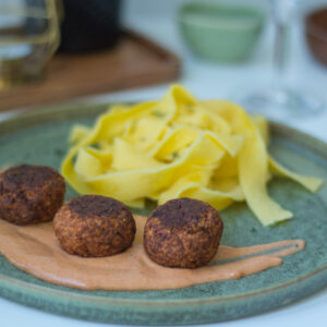 Grüner Teller mit drei vegetarischen Kürbisbällchen auf einem Klecks Schlemmersauce und daneben Bandnudeln