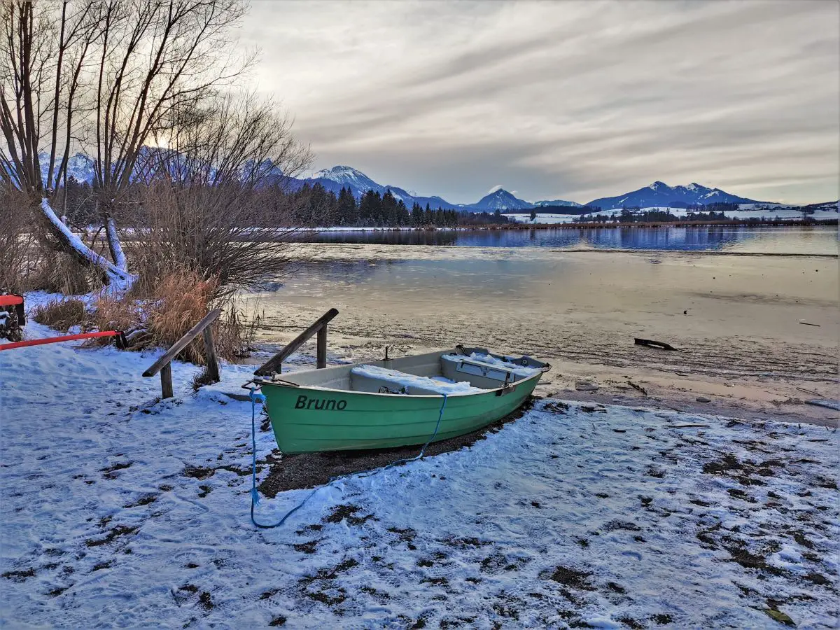 Winterspaziergang am Hopfensee in Bayern, Boot am Schnee bedeckten Ufer des Sees