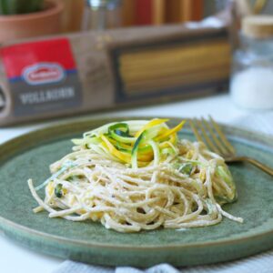 Spaghetti mit Zucchini auf einem grünen Teller, im Hintergrund Salz und Pfeffer