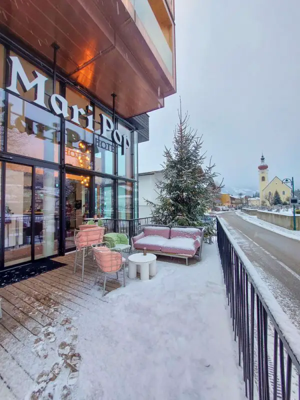 Eingang vom Mari Pop Hotel, Schnee bedeckte Terrassenmöbel und ein Tannenbaum