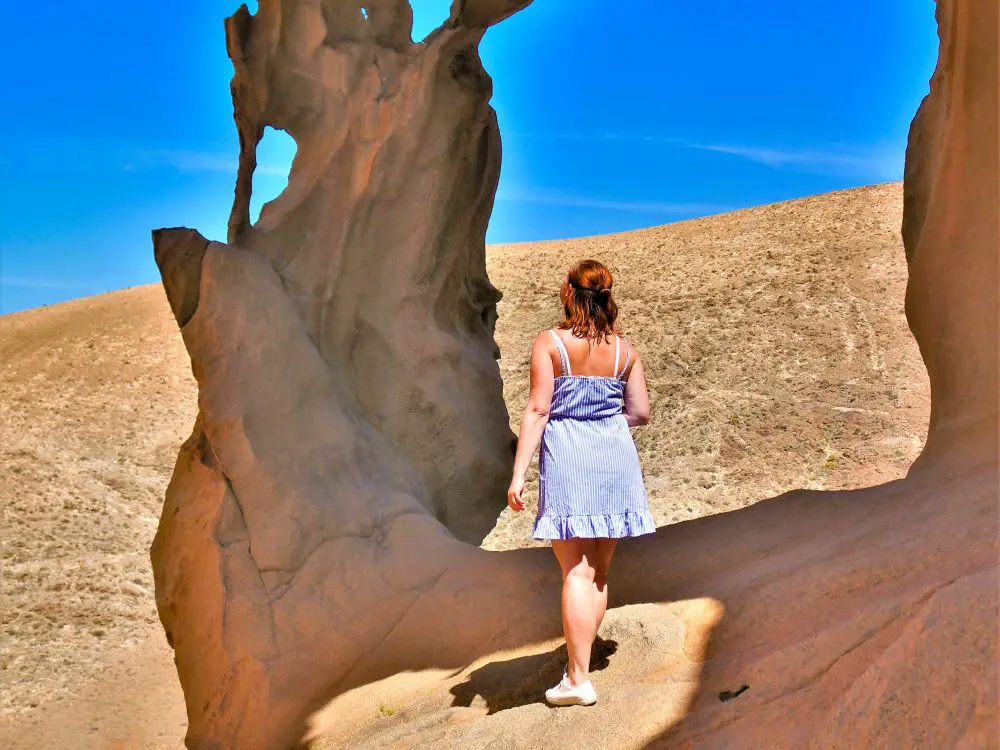 Julia steht während ihrer Reise alleine auf einem Felsen der Arco de las Peñitas. Sie hat ein blau, weißes Kleid an und bestaunt die Felsformationen.