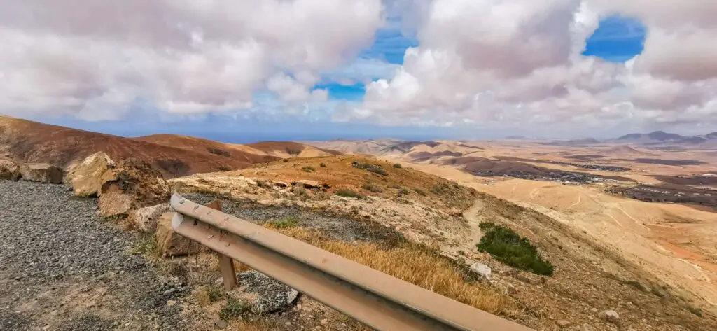 Aussicht vom Mirador Astronomico de Sicasumbre auf Fuertenventura, Kanaren. Blauer Himmel, weiße Wolken, eine karge Landschaft mit Erhebungen und dazwischen weiße Dörfer.