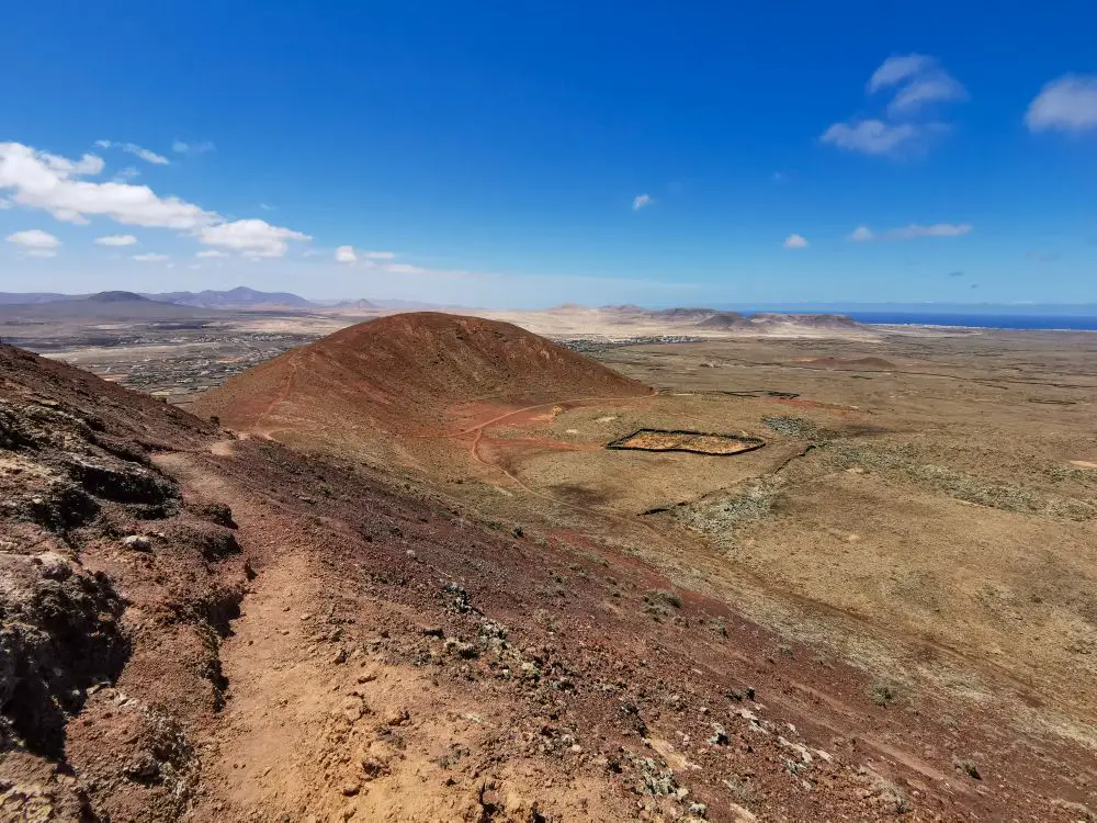 Ausblick vom Calderon Hondo, einem Vulkan auf Fuerteventura. Roter Sand, Felsen, man erkennt den Wanderweg und sieht bis zum Meer.