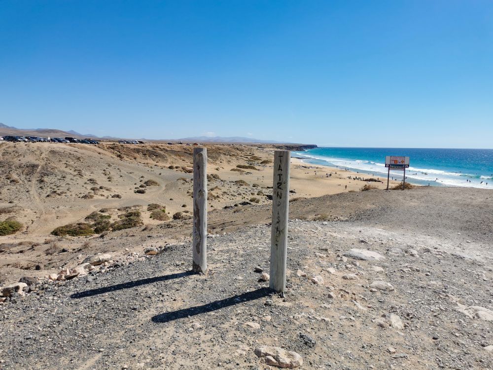 Blick von oben auf einen traumhaften Sandstrand mit Surfern im Wasser.