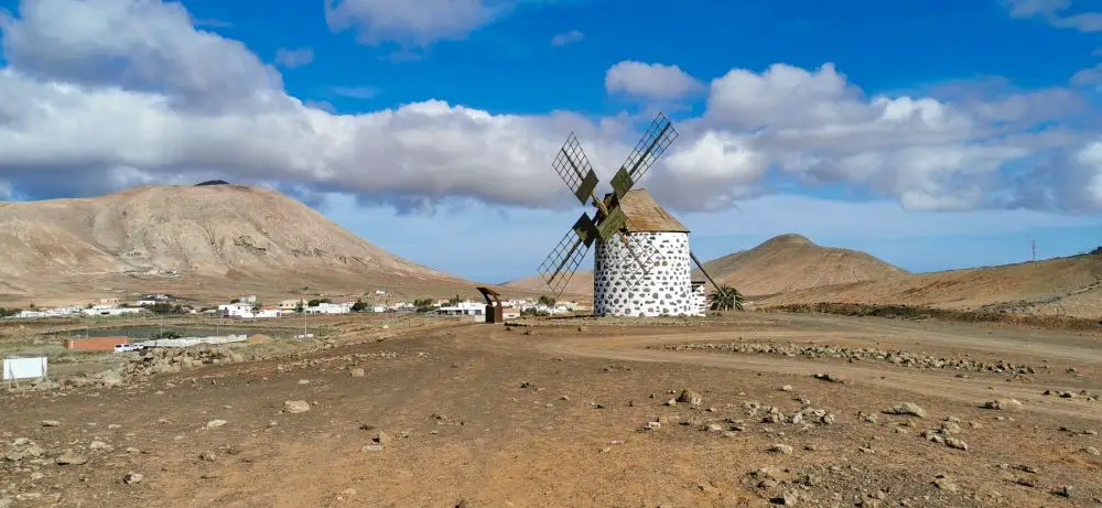 Windmühlen von Villaverde auf Fuerteventura, dahinter blauer Himmel, weiße Häuser und ein Berg.