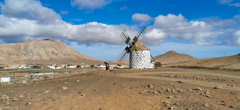 Windmühlen von Villaverde auf Fuerteventura, dahinter blauer Himmel, weiße Häuser und ein Berg.