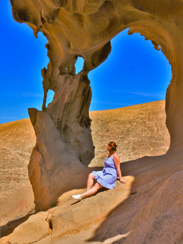 Julia steht während ihrer Reise alleine, sie sitzt auf einem Felsen der Arco de las Peñitas. Sie hat ein blau, weißes Kleid an und bestaunt die Felsformationen.