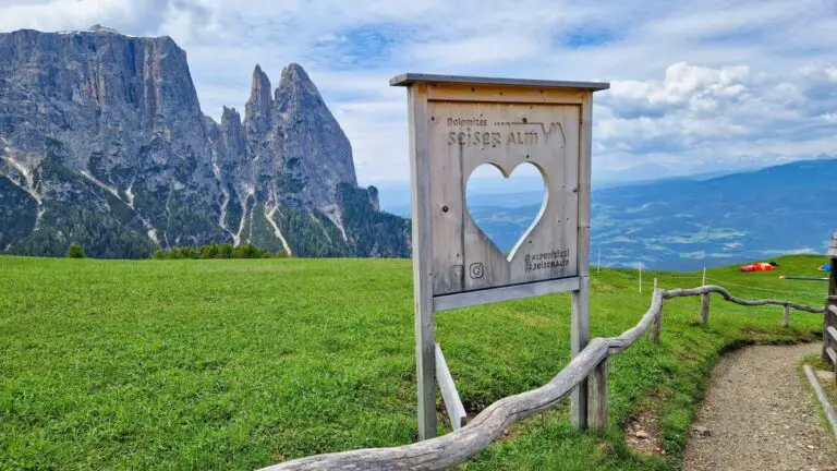 Holztafel auf der Seiser Alm mit ausgeschnittenem Herz als Fenster, dahinter die Berge der Dolomiten